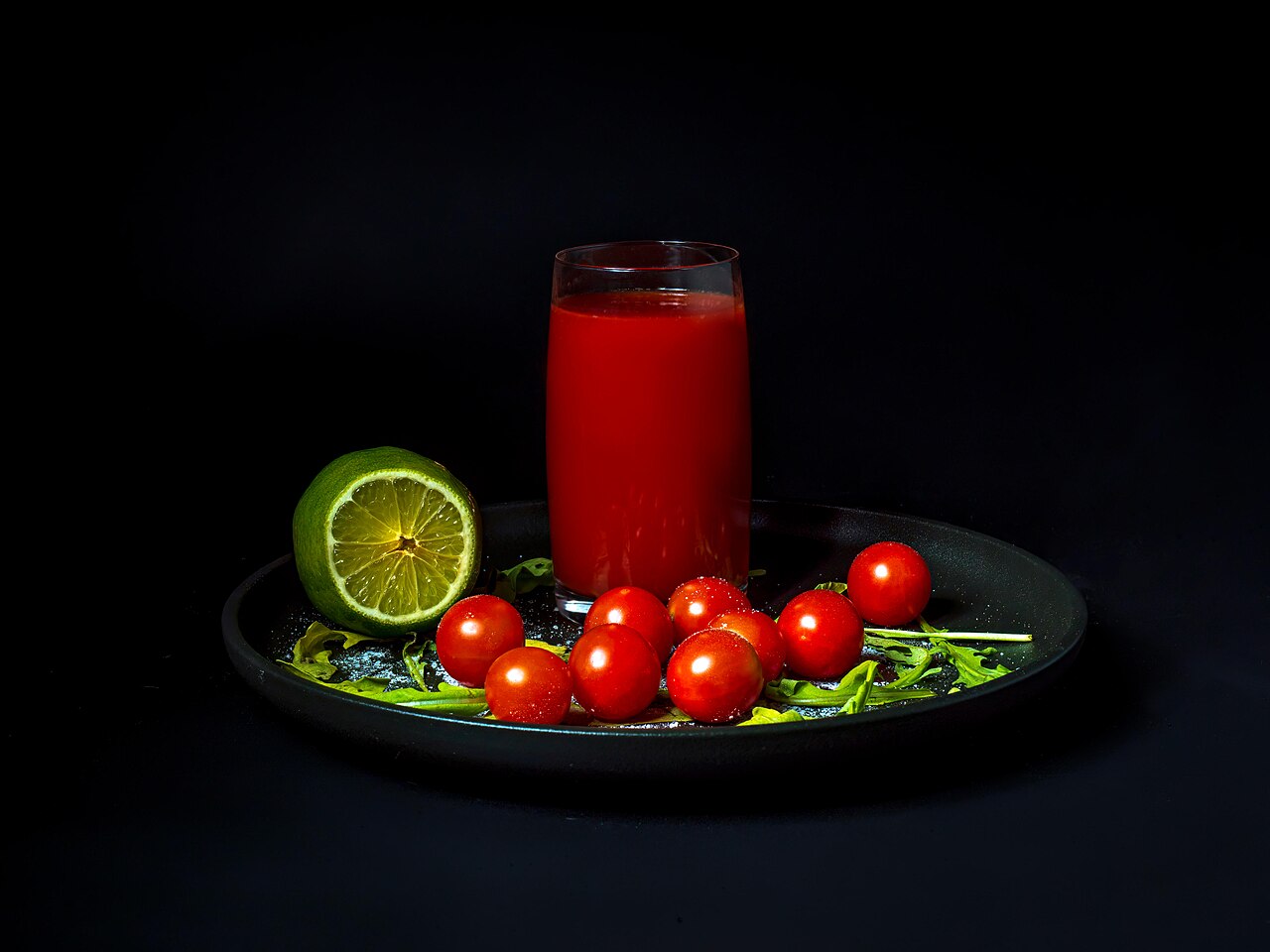 A glass of tomato juice on a black plate